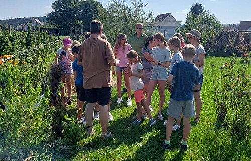 Frau Färber steht mit Kindern bei einer Führung in ihrem Garten.