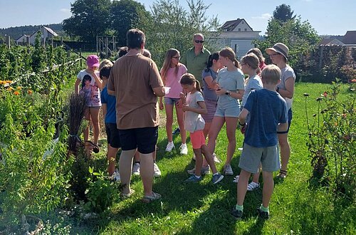 Frau Färber steht mit Kindern bei einer Führung in ihrem Garten.