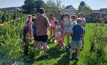 Frau Färber steht mit Kindern bei einer Führung in ihrem Garten.